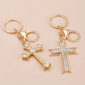Golden cross keychain pair with sparkling rhinestones on a warm beige background