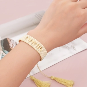 Detail of hand-woven MAMA beaded bracelet with adjustable gold tassels on wrist