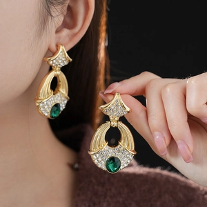 Macro shot of vintage gold earrings with green emerald pendant and diamond settings