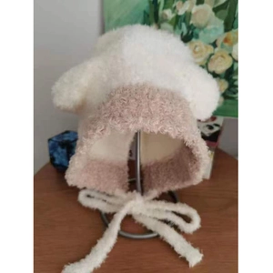 Dettaglio del cappello in peluche con paraorecchie e lunghi lacci in design bicolore