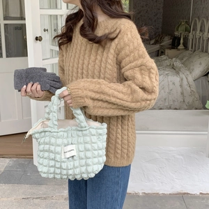 Close-up of a light green quilted bubble tote bag paired with a brown cable knit sweater