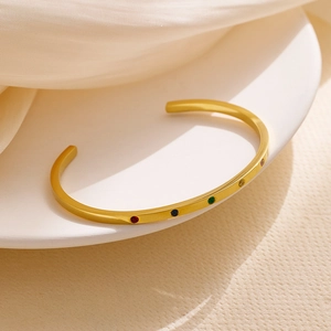 Detailed macro of gold plated C-shaped bangle with colorful zircon stones on white silk
