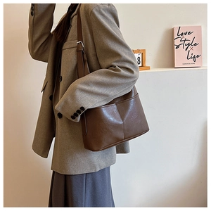 Détail d'un sac cabas marron foncé en cuir grainé porté par un mannequin en blazer chic