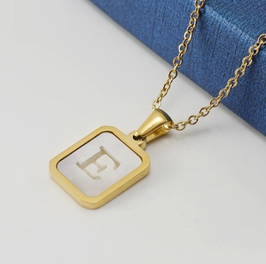 Detailed macro view of gold 18K stainless steel square pendant with white shell letter E