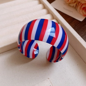 Detail of a wide acrylic cuff bracelet featuring red, white, and blue vertical stripes