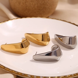 Polished 18K gold and silver hollow curved earrings displayed on white ceramic plate