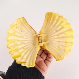 Detail showing a large shell-shaped hair claw clip in gradient yellow plastic material