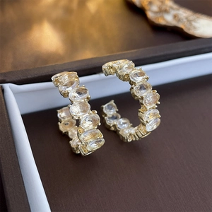 Macro shot of gold C-shaped earrings with oval rhinestones in a brown jewelry box