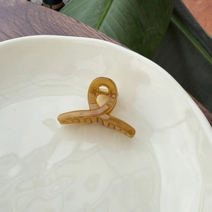 Minimalist amber resin hair clip in a twist design on a white ceramic plate