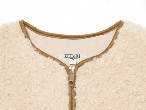Detailed macro shot of the cream fleece vest with brown trim and premium metal zipper