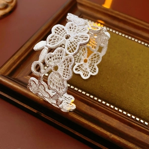 Detail eines silbernen Armreifs mit filigranem floralem Spitzenmuster und Netzelementen