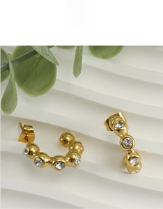 Close-up of gold U-shaped earrings with white zircons on a white textured background