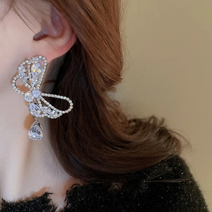 Close-up of silver bow-shaped zircon earrings with a teardrop pendant worn by a model