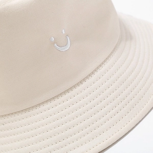 Close-up of beige cotton bucket hat showing detailed twill texture and smile embroidery
