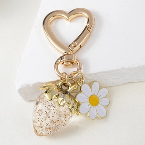 Detail of a strawberry heart keychain with golden glitter and a white daisy charm