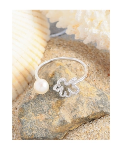 Detailed shot of open S925 silver ring featuring hollow flower and white pearl on a beach