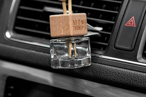 Detail of square glass perfume bottle with wooden cap and diffuser sticks in car vent