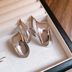 Detail view of irregular silver metal earrings with polished finish on beige velvet