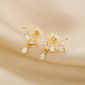 18K gold flower earrings with crystals and pearl drops on a soft beige background