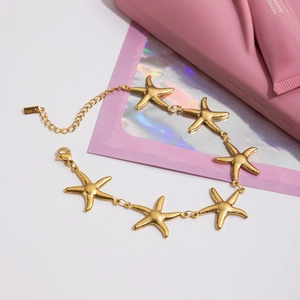 Detail of gold starfish charm bracelet with fine engraved texture and lobster clasp closure