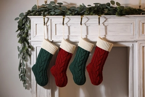 Detail of four red and green cable knit Christmas stockings hanging on a white fireplace