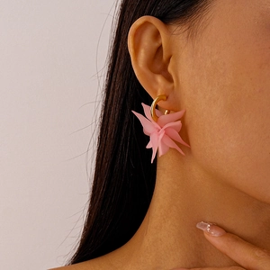 Detail of a pink acrylic flower pendant hanging from a gold-toned C-shaped earring