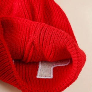 Detailed macro view of red thick knit texture and white letter patch on winter baby hat