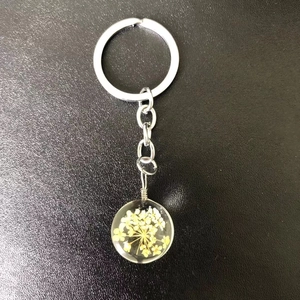 Macro view of a clear resin keychain featuring a real yellow dried flower and silver ring