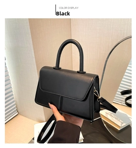 Detail of black structured crossbody bag with round handle and vertical stitching accents