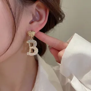 Elegant gold heart earrings with pearl and crystal encrusted letter B pendant on model