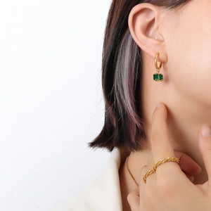 Close-up of gold twist ring and earrings with green stone charms worn by a model