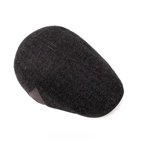 Detail view of dark grey herringbone fabric and side leather patch on newsboy cap