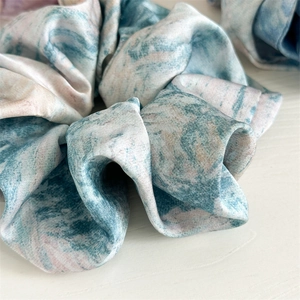 Close-up of tie-dye satin scrunchie with blue, white and pink marble pattern texture