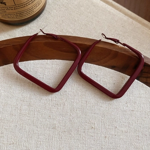 Detailed macro view of burgundy square geometric earrings on a natural wooden tray