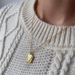 Golden square leaf texture pendant necklace displayed on a white cable knit sweater