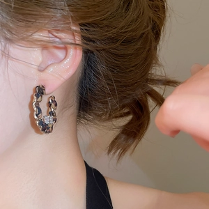 Détail macro de boucles d'oreilles en tissu léopard en C avec un grand zircon rond