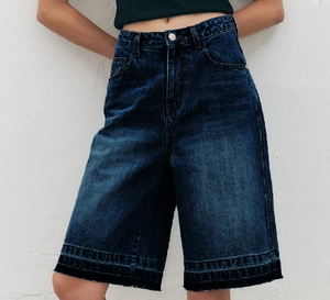 Detail of high-waisted dark blue denim Bermuda shorts with distressed frayed hem edges