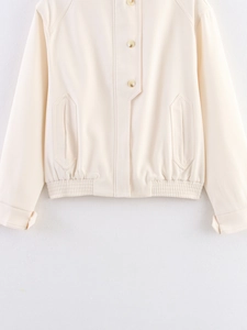 Detail of cream white jacket featuring button closure and elastic hem with geometric pockets