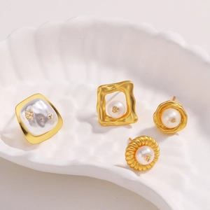 Détails de quatre boucles d'oreilles perles dorées 18k sur un plateau coquillage