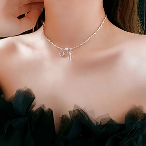 Close-up of heart necklace with pink gemstone and silver bow on model's neckline