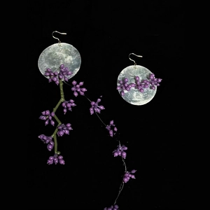 Detail of asymmetrical shell flower earrings with purple beads and long green vine tassels