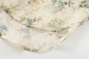 Détail de l'ourlet arrondi d'une chemise à fleurs crème avec boutons dorés élégants