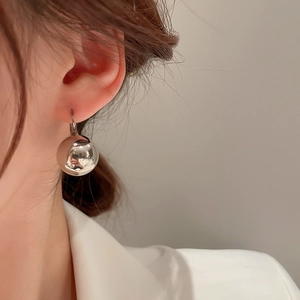Gros plan d'une boucle d'oreille boule argentée minimaliste portée par un mannequin