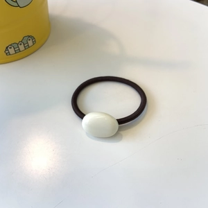 Detail view of a minimalist brown elastic hair tie with a creamy white oval accent piece