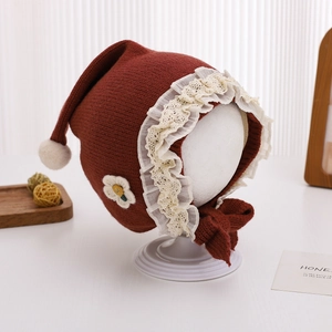 Detailed close-up of baby lace bonnet with floral applique and plush pom-pom decoration