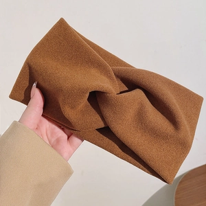Gros plan d'un bandeau en tissu marron torsadé tenu à la main sur fond épuré