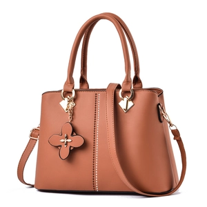Caramel brown leather trapezoid handbag with beaded lines and a clover charm accessory