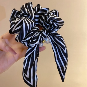 Detailed view of striped satin scrunchie with long bow, pearl charms and gold accents