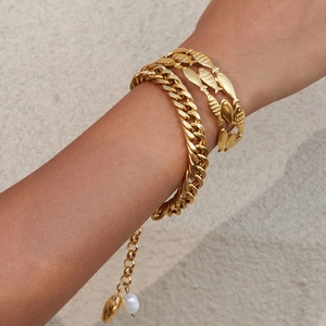 Golden Cuban link and fish pattern layered bracelets with pearls on a model's wrist