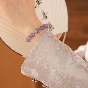 Detail of amethyst beaded bracelet with silver charm worn against a vintage fan